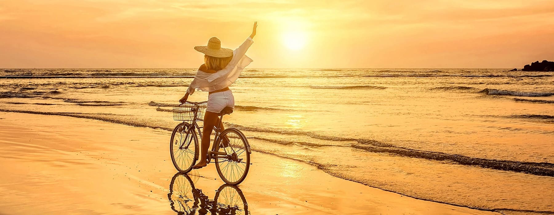 lifestyle image of a person riding a bicycle on the beach at sunset
